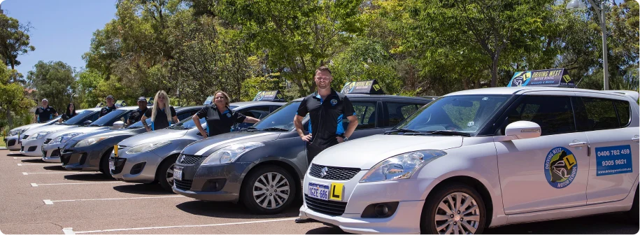 Driving West instructor team and training cars Driving West instructors standing beside their branded lesson cars